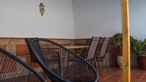 A patio area with wicker chairs and a wooden table, surrounded by potted plants and a tiled floor. - Casa Rural El Patio, with private pool (Fuente de Piedra)