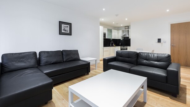 A modern living room with two black leather sofas, a white coffee table, and a kitchen area in the background. - Beautiful 1 bedroom apartment (Croydon)