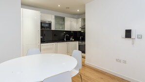 A modern kitchen with white cabinets, a black countertop, and a round white table with chairs. - Beautiful 1 bedroom apartment (Croydon)