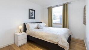 A bedroom with a bed, a nightstand, a framed picture on the wall, and a window with curtains. - Beautiful 1 bedroom apartment (Croydon)