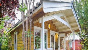 Una casa de madera amarilla con un porche cubierto, sillas blancas y una pequeña mesa.