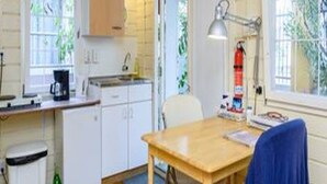Cocina compacta con armarios blancos, una mesa de madera y una ventana con vistas a zonas verdes.