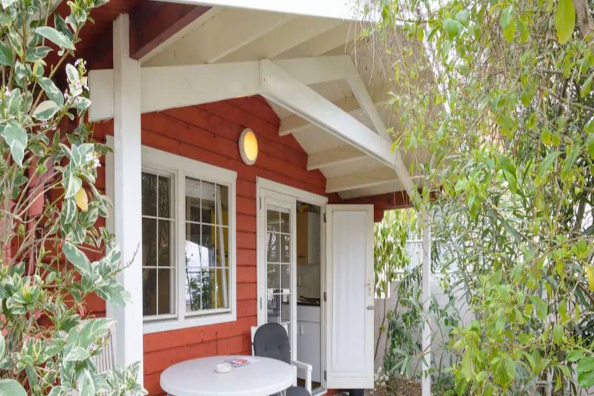 A covered patio with a round table and two chairs, a red exterior wall, and a door leading to an interior space.