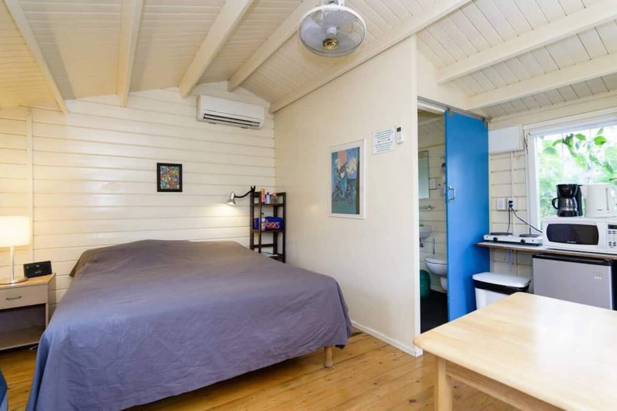 A bedroom with a bed, bedside table, lamp, and a small shelf with books.