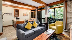 Ein modernes Wohnzimmer mit einem grauen Sofa, gelben Sesseln, einem Holztisch und einem Essbereich, wobei im Hintergrund eine Küche zu sehen ist.