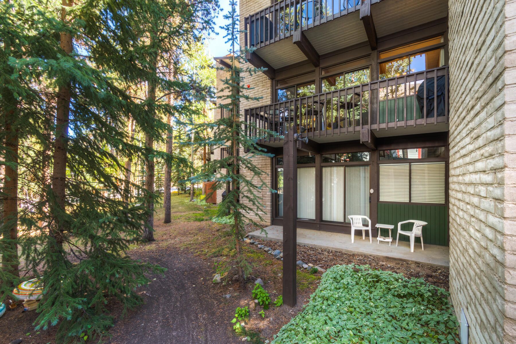 A multi-story building with a balcony, outdoor seating, and a forested area.