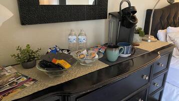 A hotel room with a minibar, a coffee maker, a potted plant, and a bed with white linens.