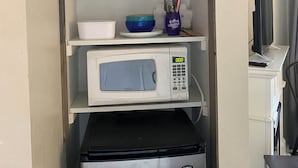 Une petite cuisine équipée d’un four à micro-ondes, d’un réfrigérateur et d’étagères contenant des ustensiles de cuisine et des objets de décoration.