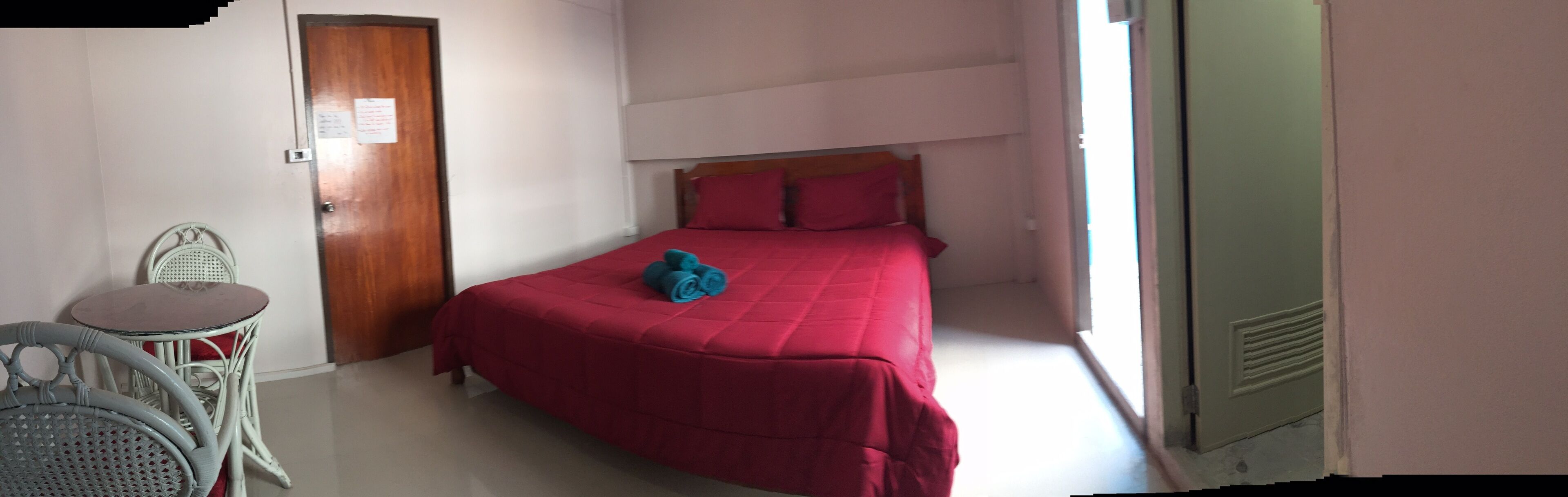 A small, neatly arranged bedroom with a single bed, a wooden door, a small table, and a chair.