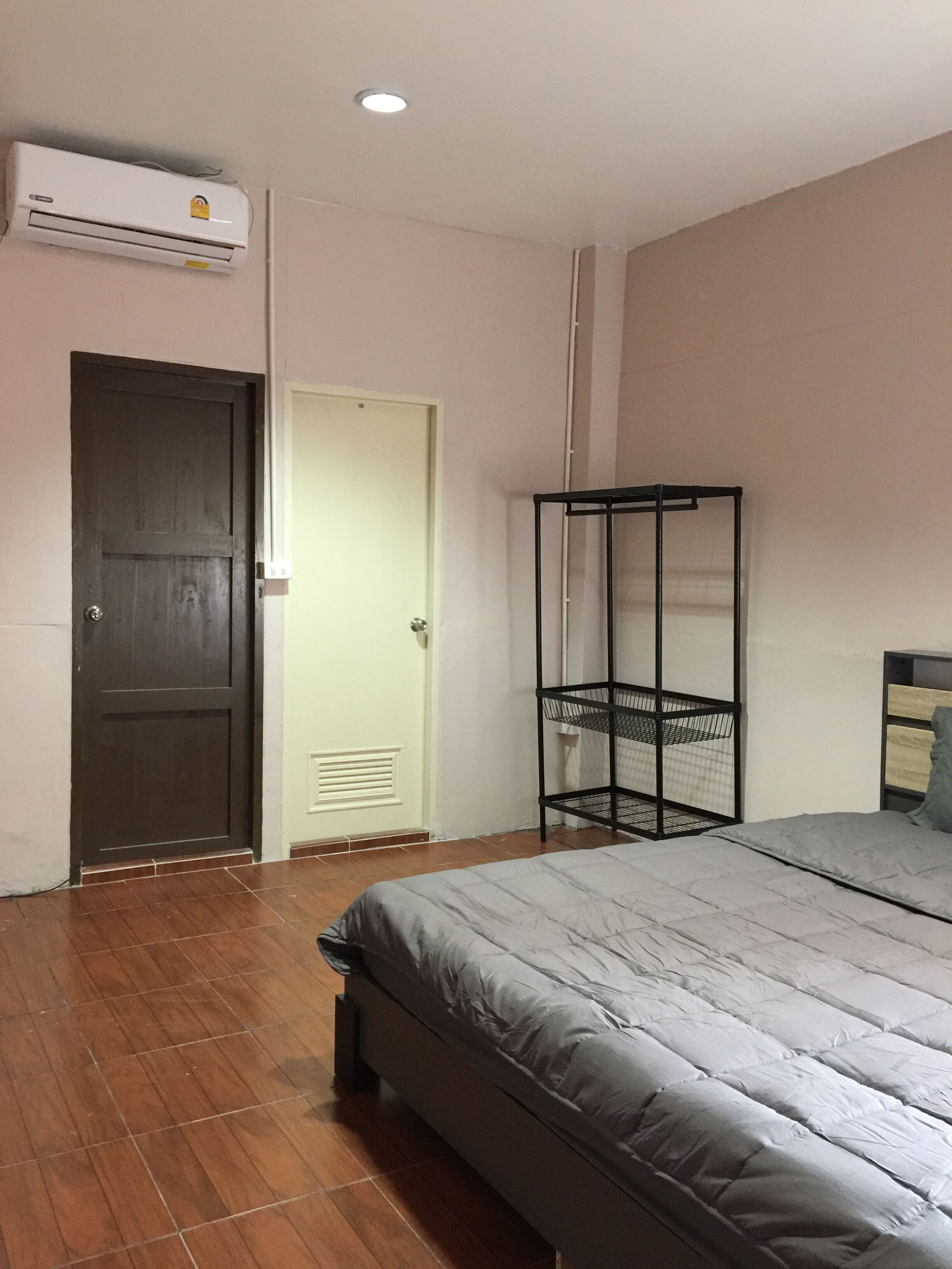Un dormitorio con cama, armario, estantería metálica negra, equipo de aire acondicionado y una puerta.