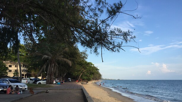 A beach with a paved walkway, parked cars, and a view of the sea. - Smile Home Guesthouse (Rayong)
