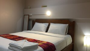A neatly made bed with white linens, a folded towel, and a red and orange patterned blanket. A 'No Smoking' sign is visible on the wall above the bed. - Smile Home Guesthouse (Rayong)