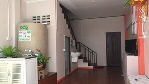 A spacious living area with a staircase, a white cabinet with plants, and a sign indicating a new upgrade. - Smile Home Guesthouse (Rayong)