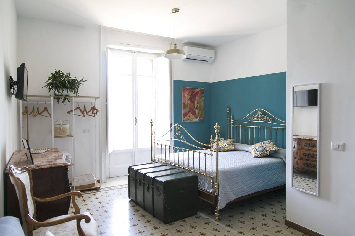 Une chambre à coucher comprenant un lit, une commode, un bureau, une chaise, une plante suspendue et une fenêtre.