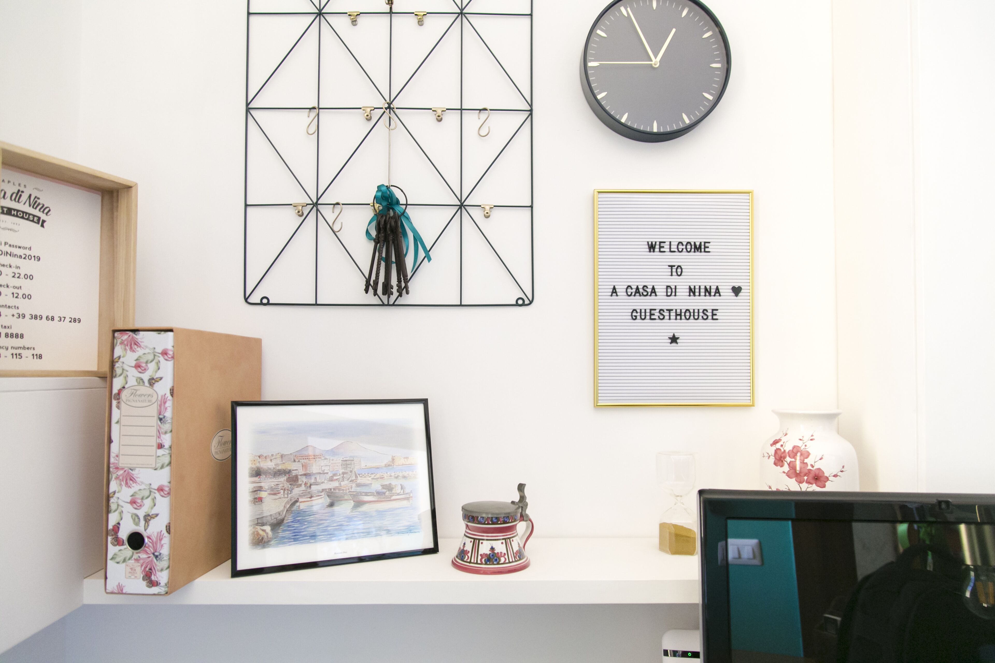 A wall with a clock, a welcome sign, a framed picture, a decorative item, and a framed menu.