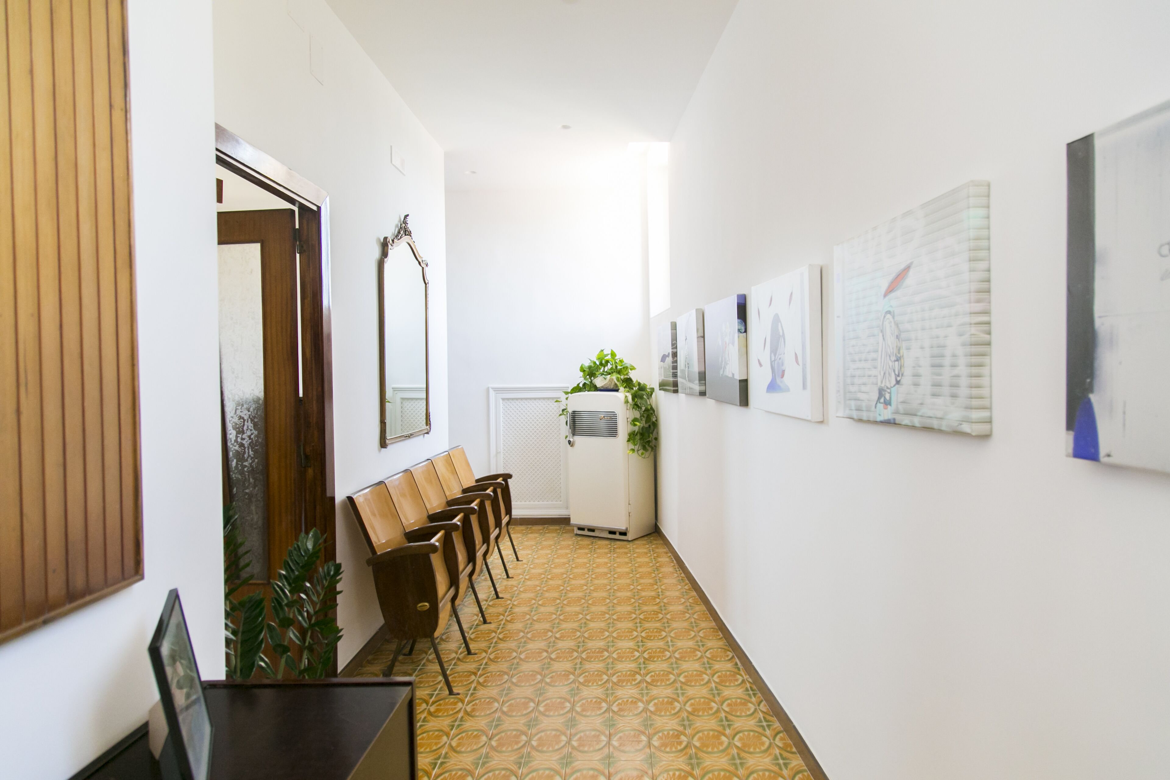 A hallway with a patterned floor, wooden benches, a white radiator, and framed artwork on the walls.