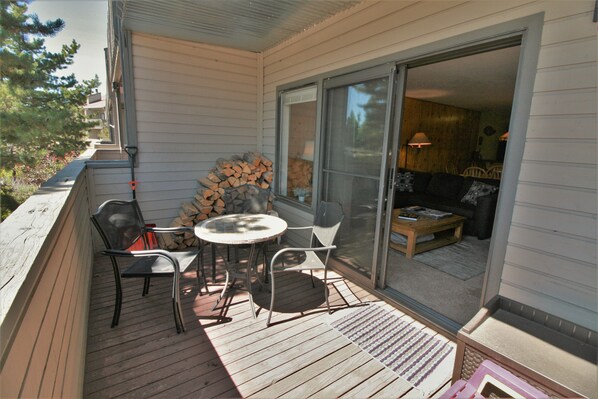 A covered patio with a table and chairs, a stack of firewood, and a sliding glass door leading to an interior living space.
