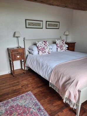 A bedroom with a wooden floor, a bed with white bedding and pink accents, two nightstands with lamps, and a patterned rug.