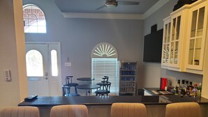 A bar area with a counter, bar stools, and a seating area with tables and chairs. - Modern Home in Excellent Location!! (Fort Worth)