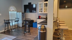 A modern kitchen with a dining area, bar stools, and a TV mounted above the counter. - Modern Home in Excellent Location!! (Fort Worth)
