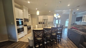 A modern kitchen with white cabinetry, stainless steel appliances, and a central island with bar stools. - Modern Home in Excellent Location!! (Fort Worth)