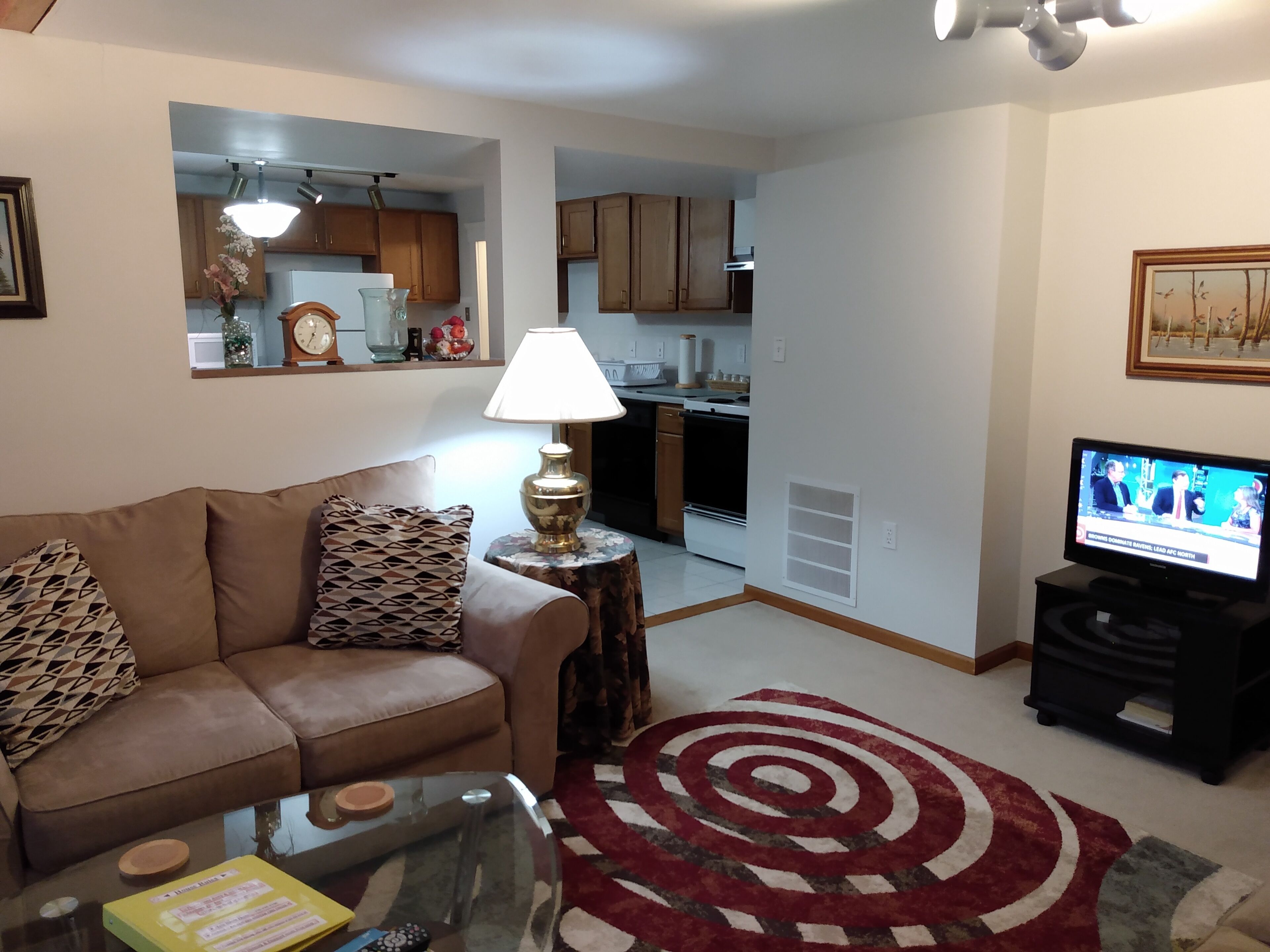 A living room with a sofa, a coffee table, a TV, and a kitchen in the background.
