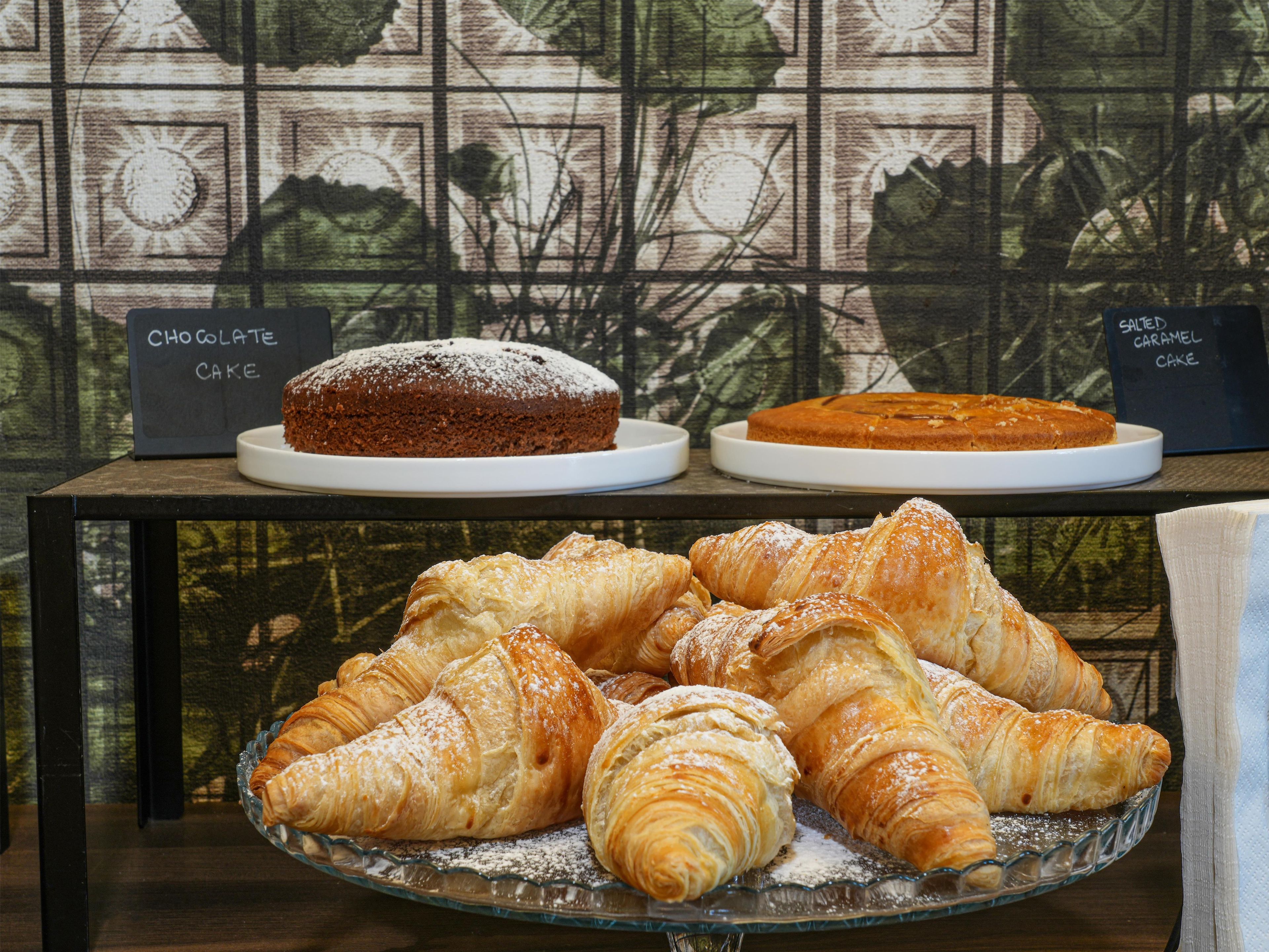 Una exhibición de postres que incluye pastel de chocolate, pastel de caramelo salado y croissants sobre una mesa con un fondo estampado.