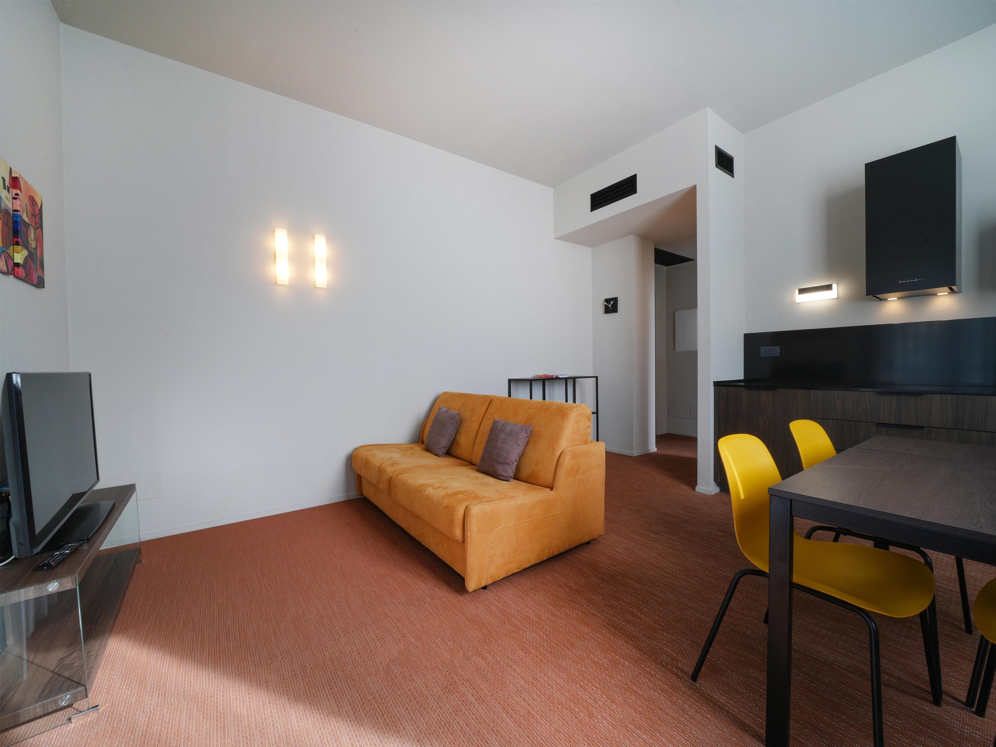 Un salon moderne comprenant un canapé, une table à manger avec des chaises, un téléviseur à écran plat et un coin cuisine équipé d’un four à micro-ondes.