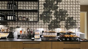 Een bar met flessen op planken, een koffiemachine en diverse etenswaren.