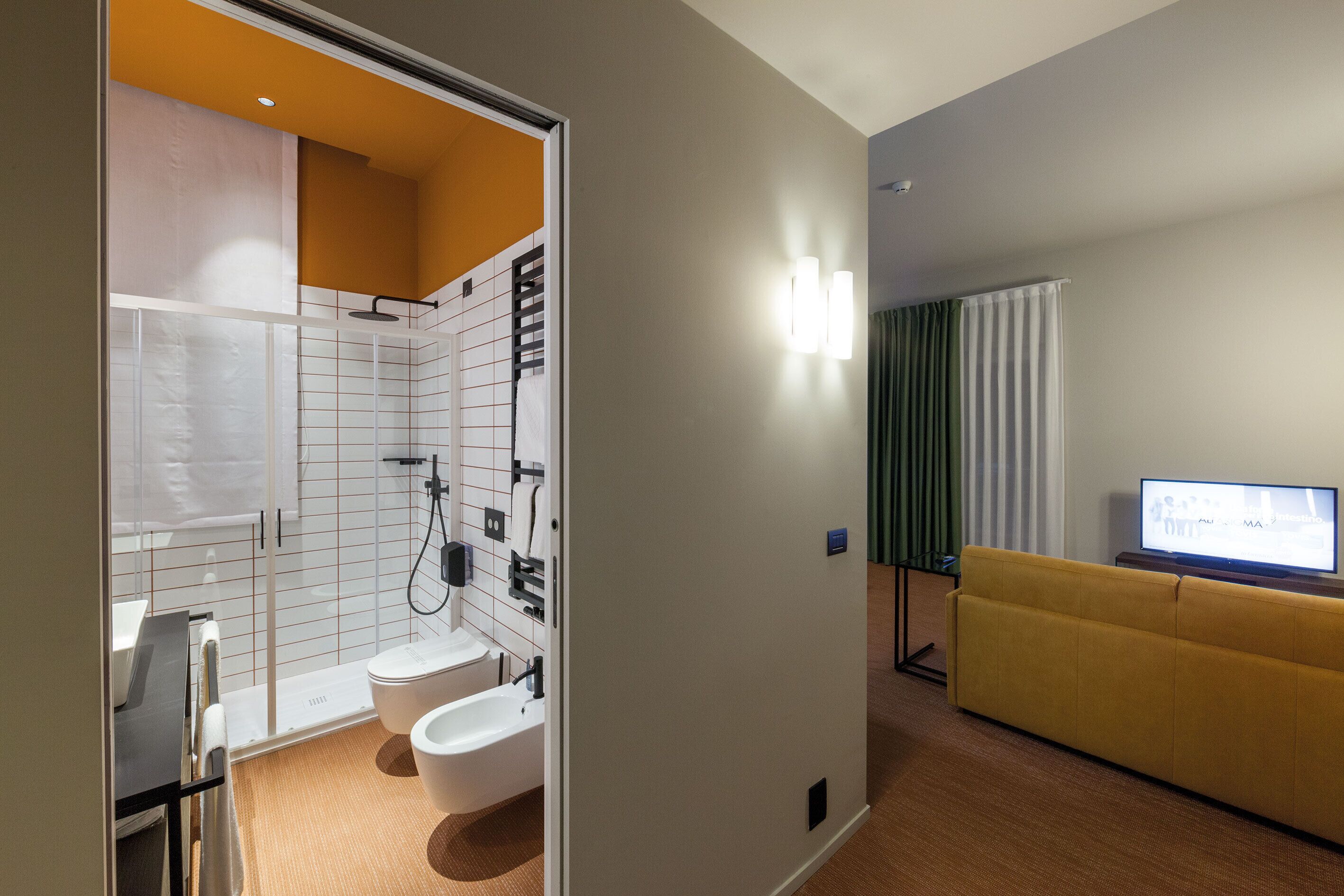 Un baño moderno con ducha, inodoro y lavamanos. En la sala de estar, hay un sofá amarillo y un televisor de pantalla plana.