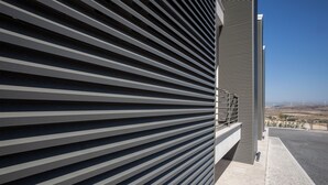 Een modern gebouw met horizontale lamellen aan de gevel, een verharde looppad en een verre weide uitzicht op windmolens.