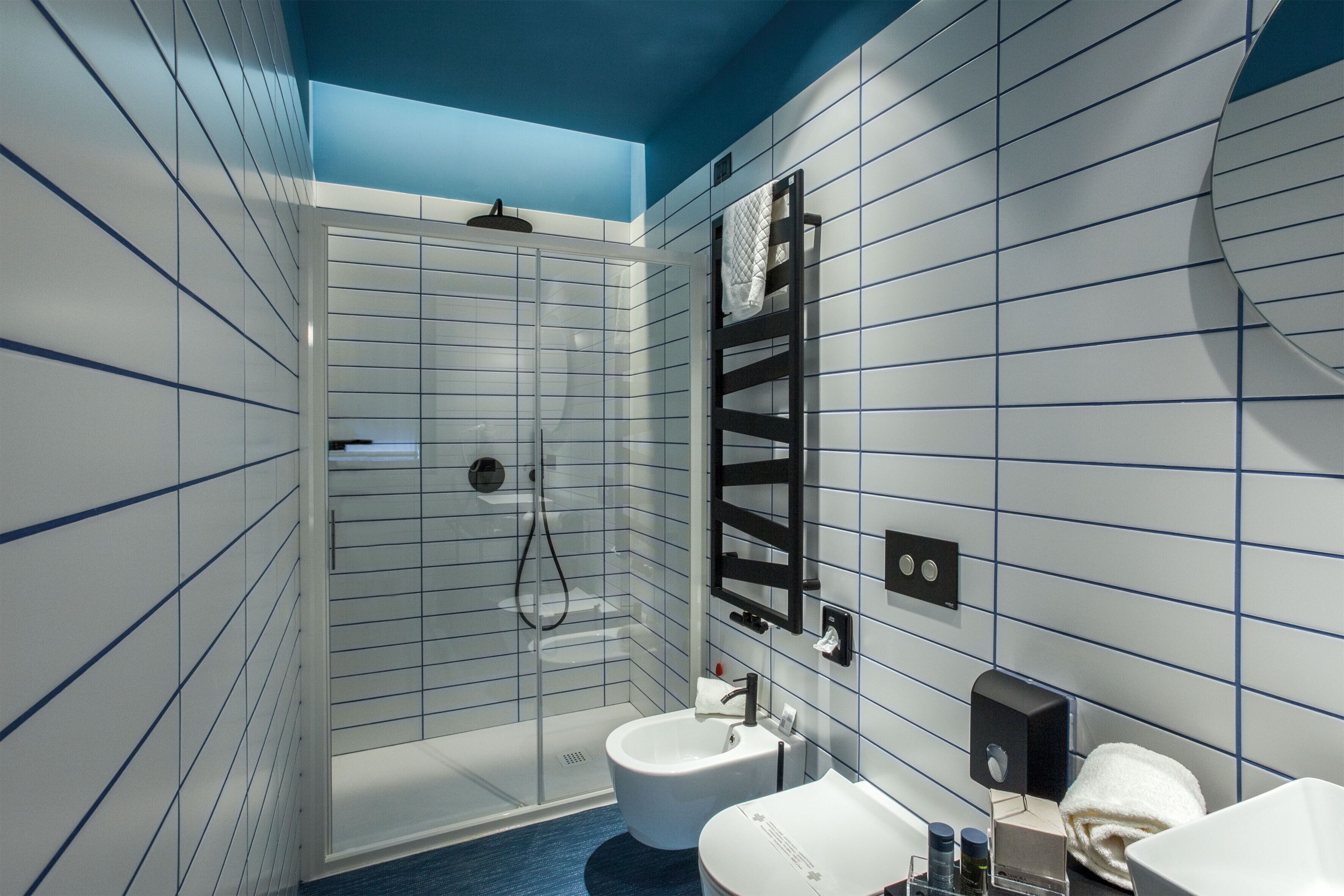 Un baño moderno con ducha envuelta en vidrio, un lavamanos blanco y un perchero para toallas.