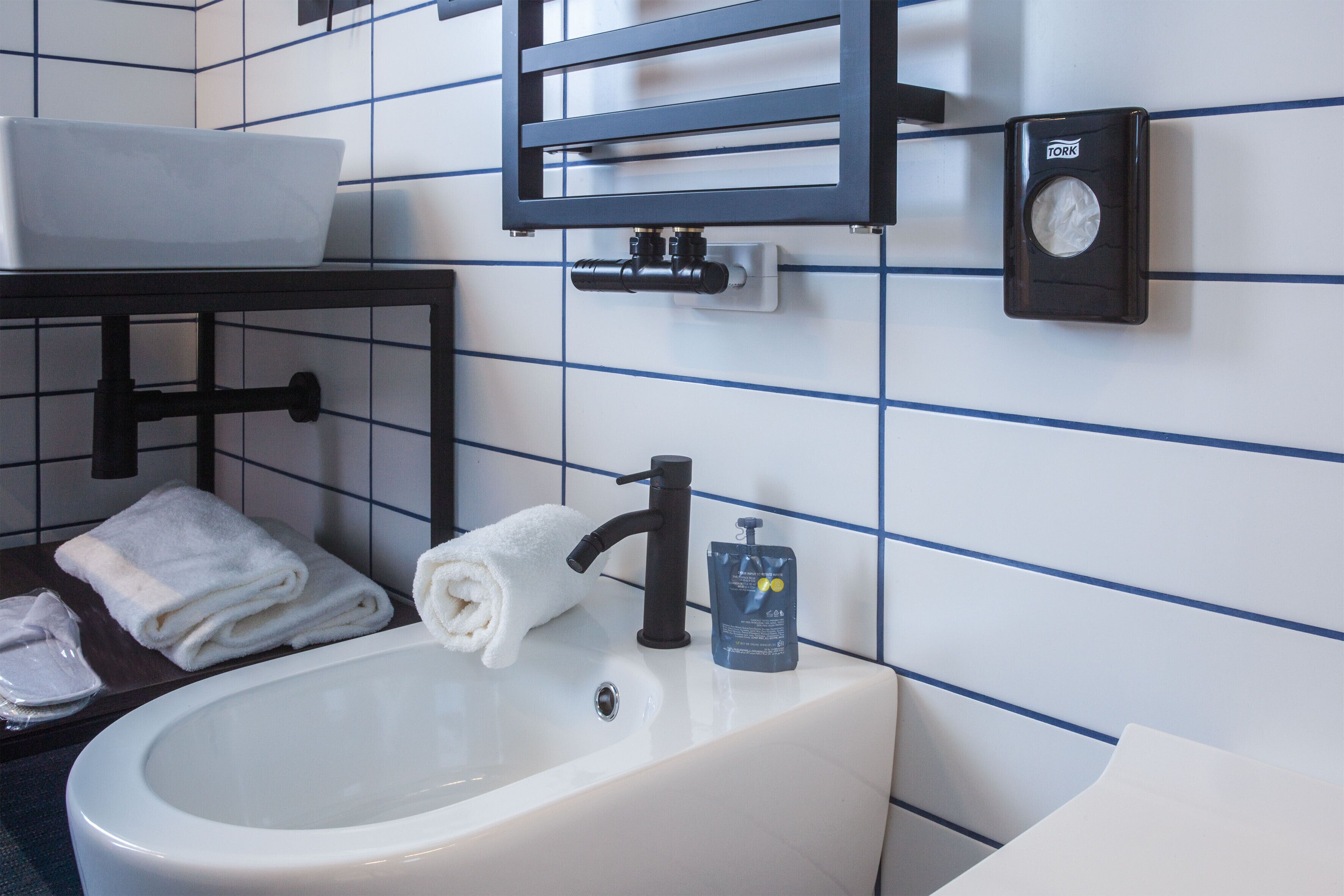 A bathroom with a white sink, a towel rack, a soap dispenser, and a toilet paper holder on the wall.