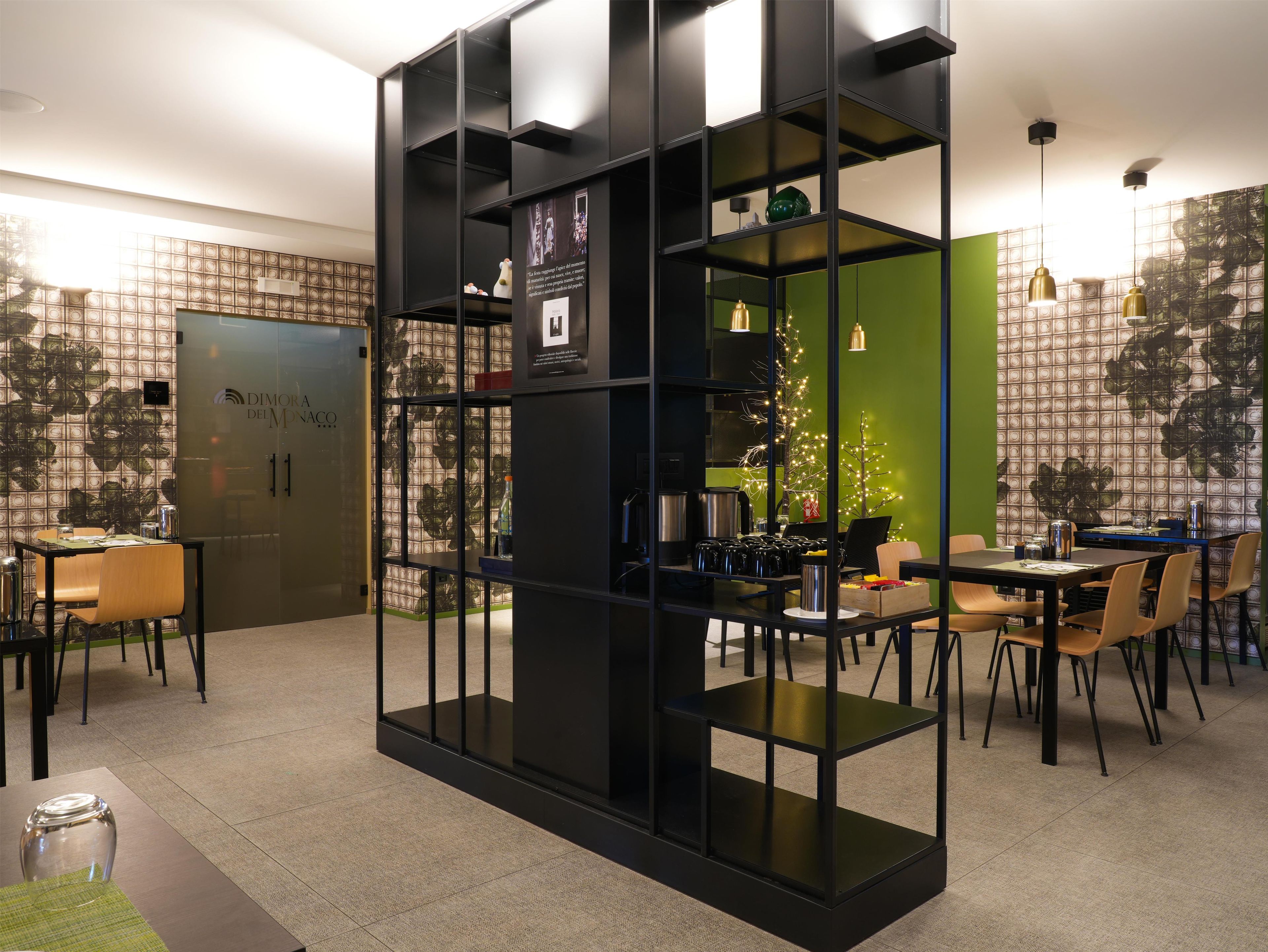 A modern dining area with a black shelving unit, a green accent wall, and a glass partition.