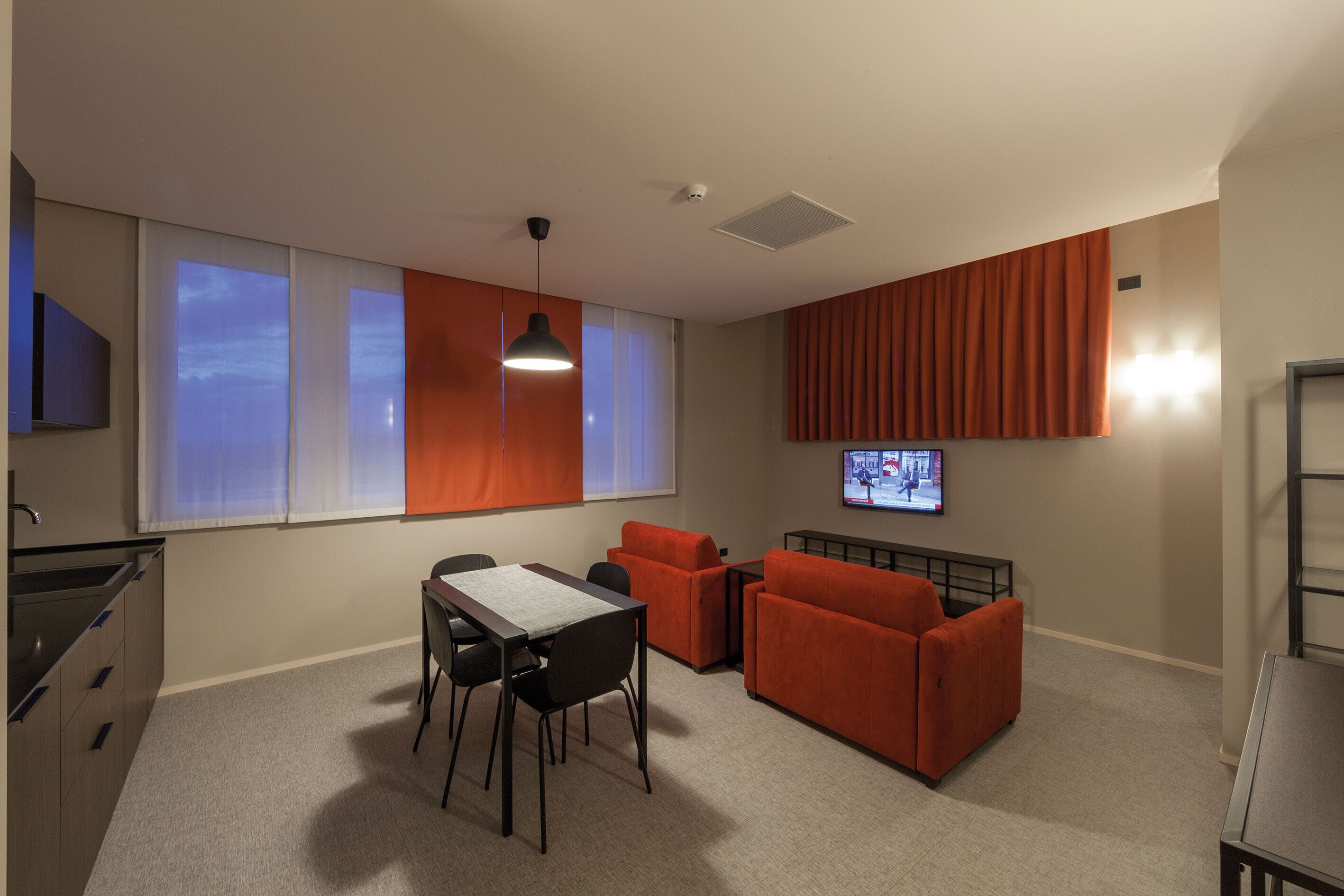Una sala de estar moderna con comedor, muebles naranjas, televisor de pantalla plana y área de cocina.