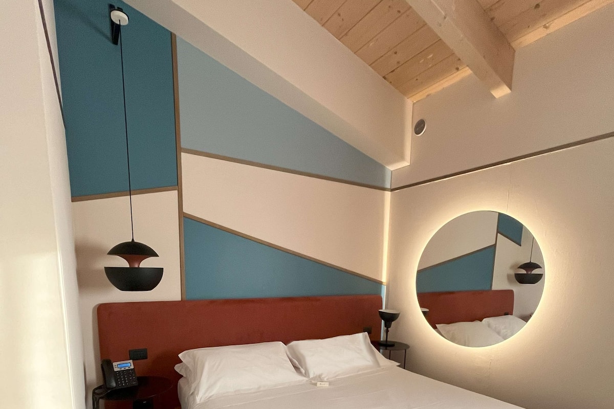 A modern hotel room with a large bed, a bedside phone, and a round mirror on the wall.