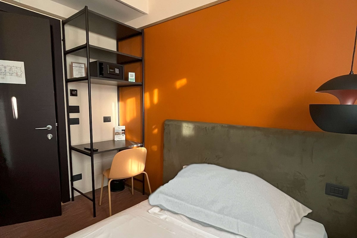 A hotel room with a bed, a desk, a chair, and a wardrobe.