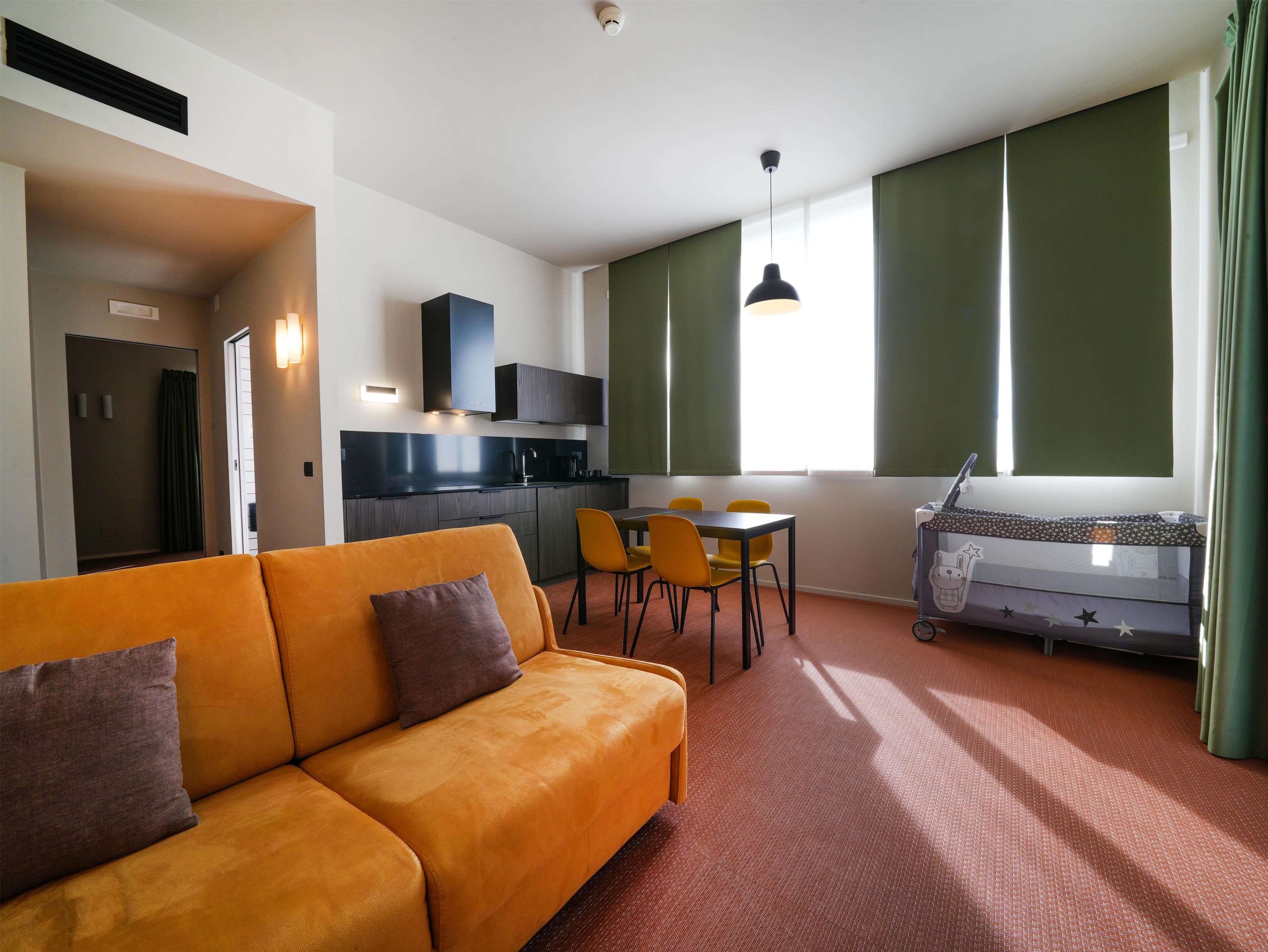 Una sala de estar moderna con un sofá, una mesa de comedor con sillas, una kitchenette y una ventana con cortinas.