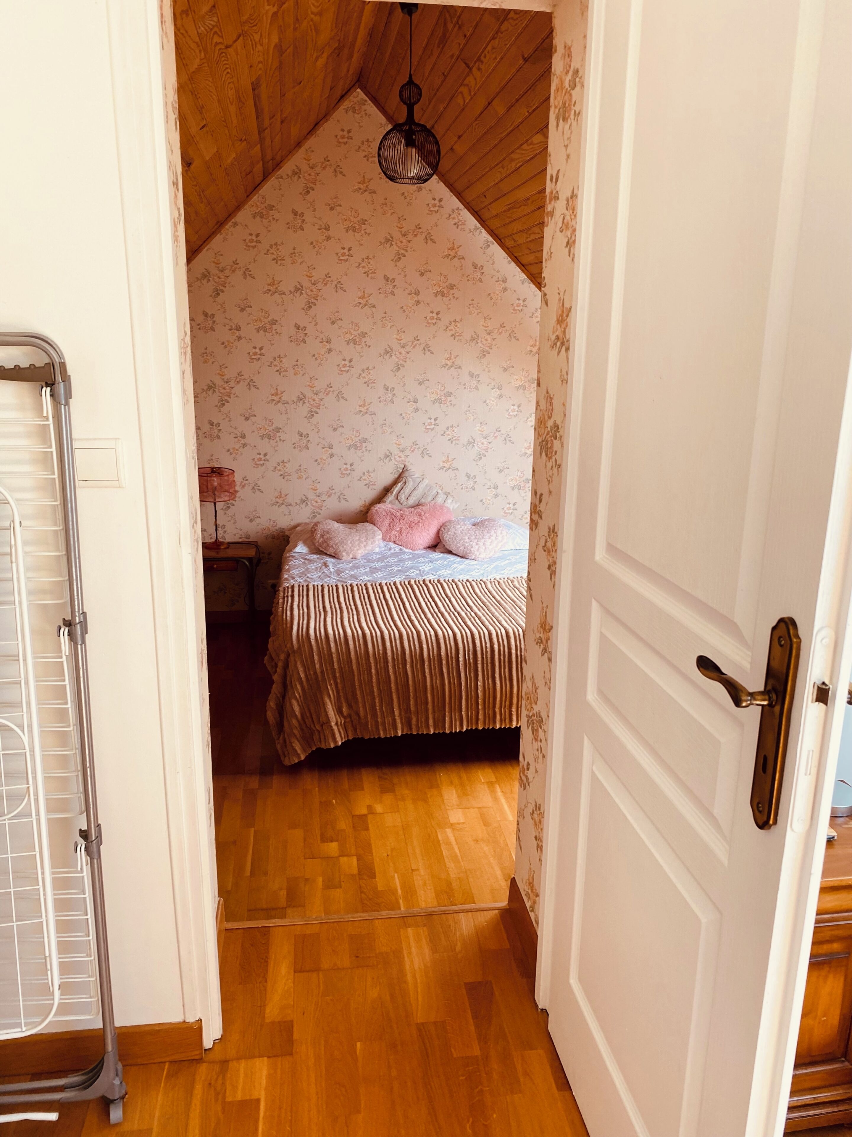 Un dormitorio con techo de madera, una cama con cabecera estampada con motivos florales y una lámpara colgante.