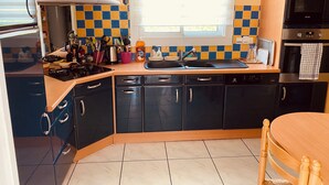 A kitchen with a stove, sink, and cabinets, a window with blinds, and a microwave. - House close to the beach (Carnac)