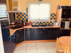 A kitchen with a stove, sink, and cabinets, a window with blinds, and a microwave.