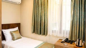 Quarto de hotel com cama, mesa de cabeceira, telefone, chaleira e cortinas.
