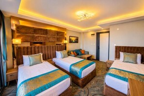 Habitación de hotel con dos camas, un sofá, un escritorio y un cabecero con televisor integrado.