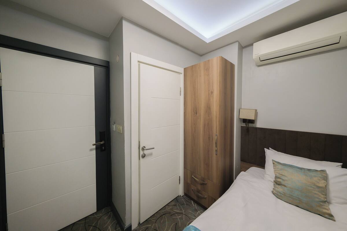 A hotel room with a bed, a wardrobe, a door, and an air conditioning unit.
