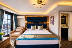 A hotel room with a large bed, a seating area with a chair, a wall-mounted air conditioner, and a view through a window. - Grand Kavi Hotel (Istanbul)