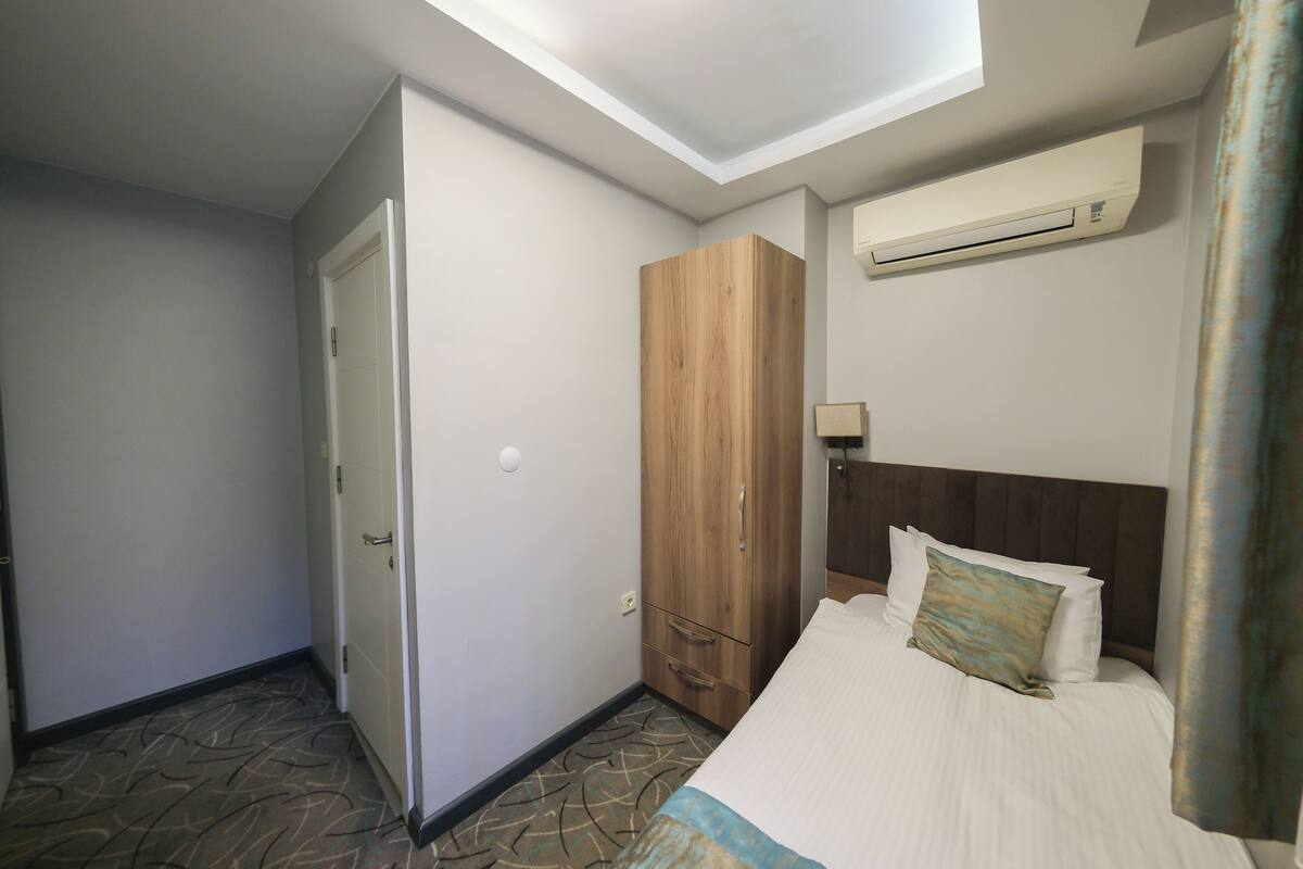 A hotel room with a bed, a wardrobe, a ceiling light, and an air conditioning unit.