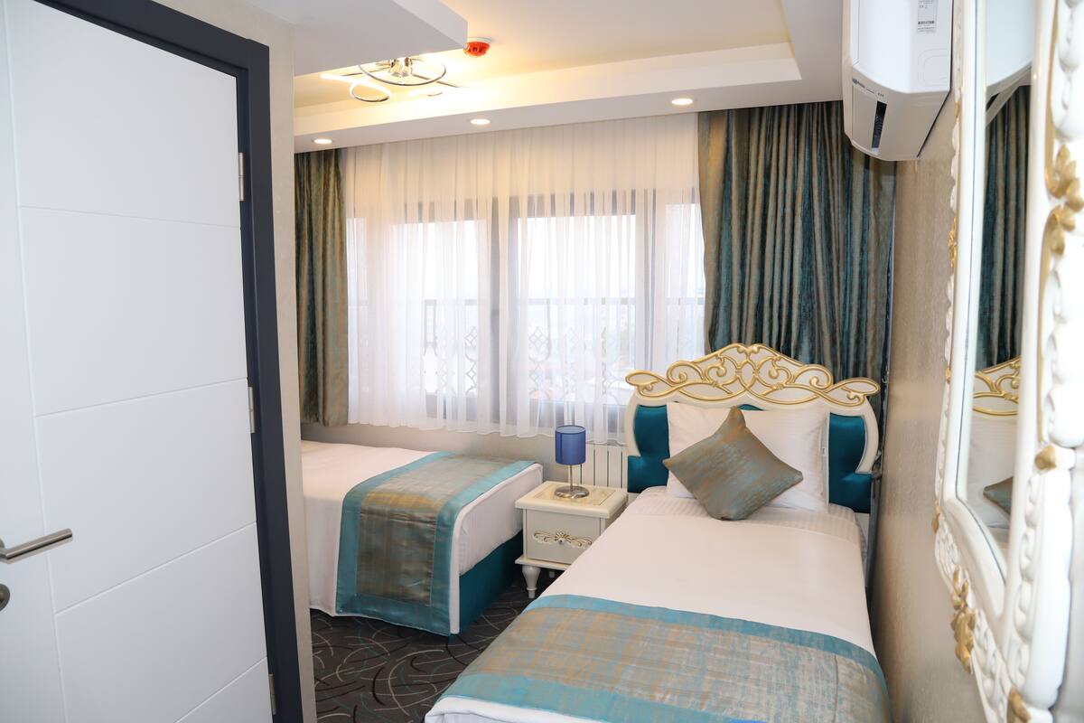 A hotel room with two beds, a nightstand, a mirror, and a window with curtains.