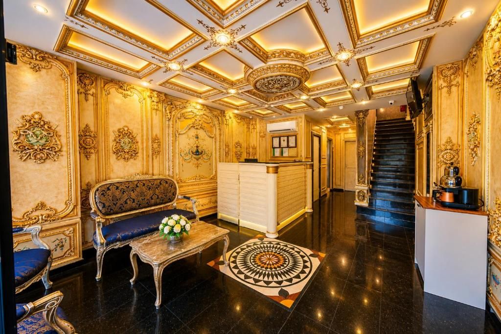 Un vestíbulo opulento con detalles ornamentales dorados, una imponente escalera y una recepción.