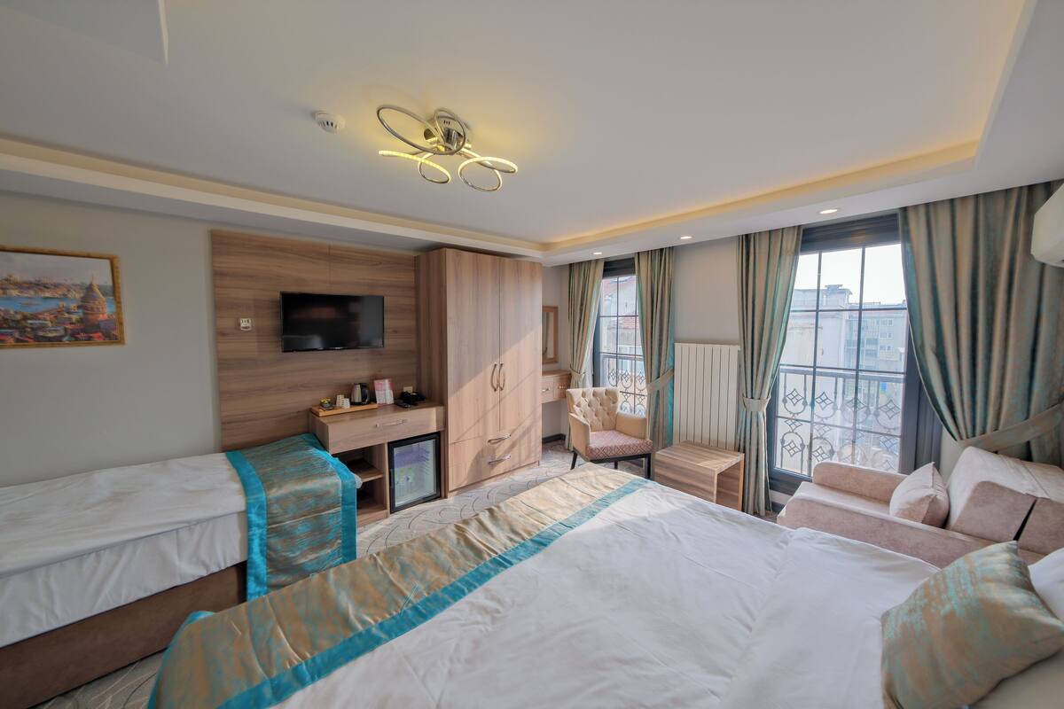 A hotel room with a bed, a desk, a chair, a TV, and a window with curtains.