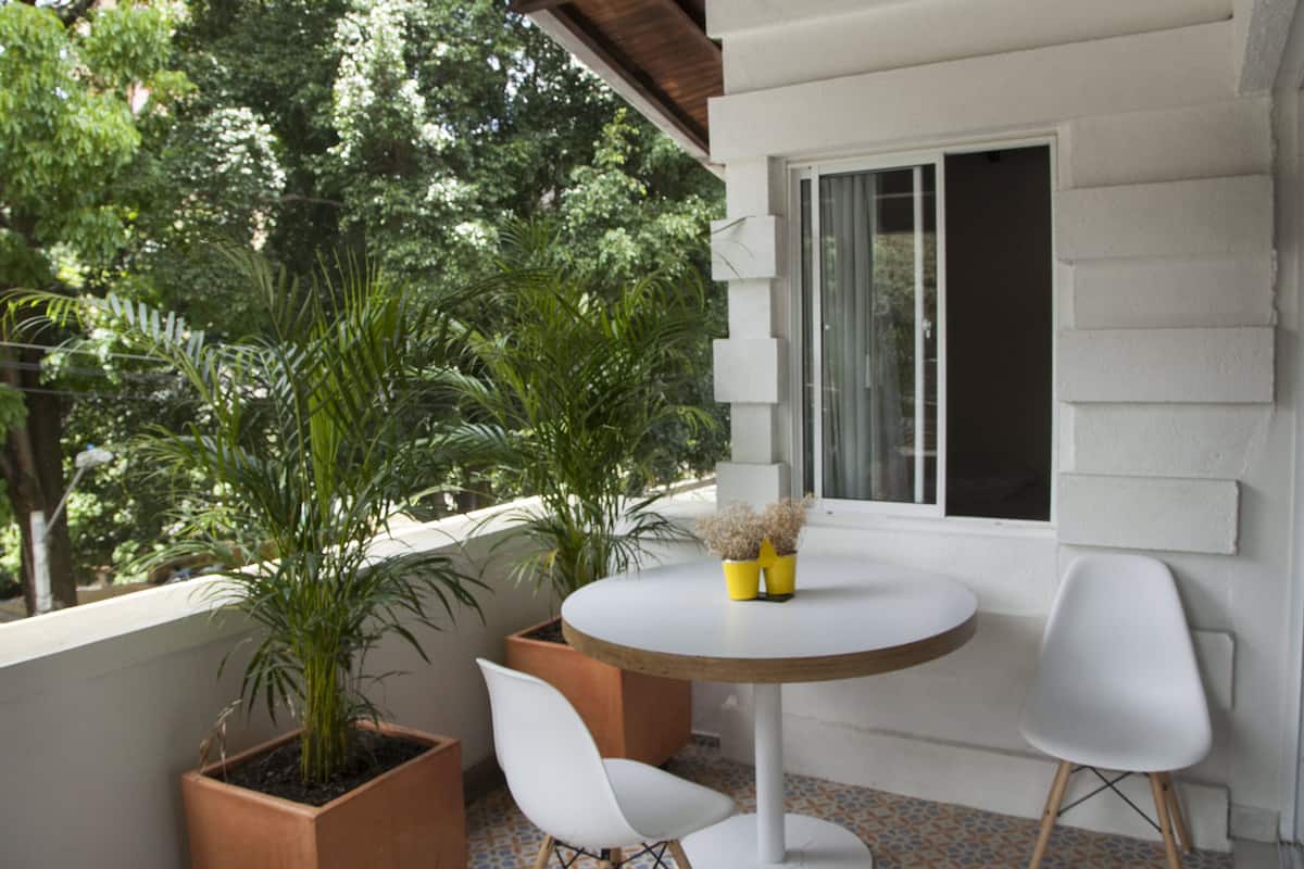 Un balcón con una mesa redonda, dos sillas blancas y plantas en macetas.
